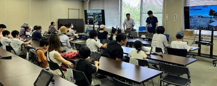 Senior Researcher DENDA Masatoshi and Researcher YAMASHITA Daiki (standing in the back) explaining the activity to participants.