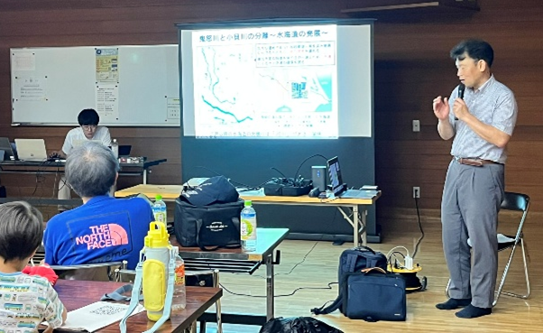 Senior Researcher DENDA Masatoshi and Researcher YAMASHITA Daiki (standing in the back) explaining the activity to participants.